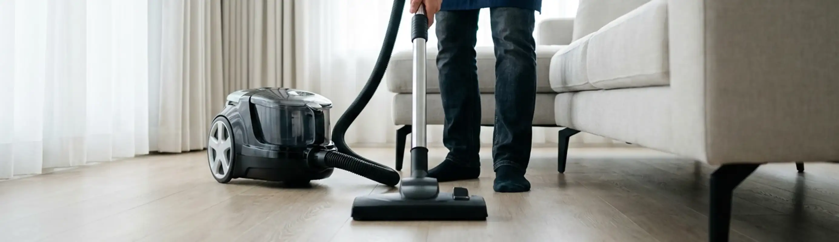 Professional house cleaner vacuuming a living room floor with a canister vacuum cleaner, Manchester, NH.