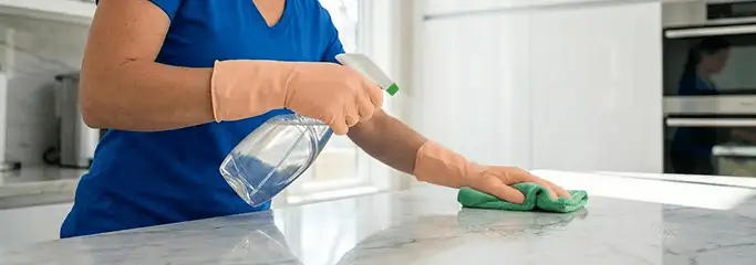 Maid service worker spraying and wiping a kitchen countertop with a microfiber cloth for sanitizing, Manchester, NH.