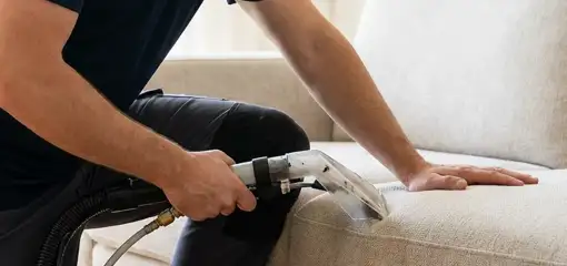 Professional upholstery cleaner deep-cleaning a fabric sofa with a handheld extraction tool, Manchester, NH.
