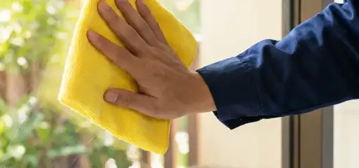 House cleaner wiping a glass window with a yellow microfiber cloth for streak-free cleaning, Manchester, NH.